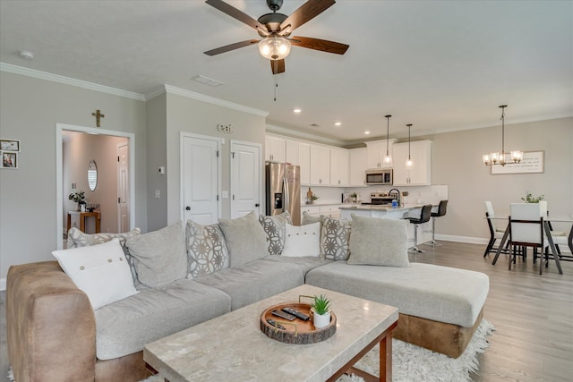 living room with light wood-style floors, baseboards, crown molding, and ceiling fan with notable chandelier