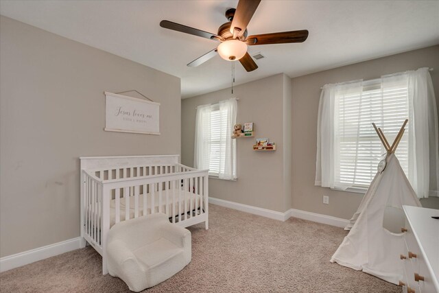 carpeted bedroom with a crib, baseboards, a ceiling fan, and visible vents