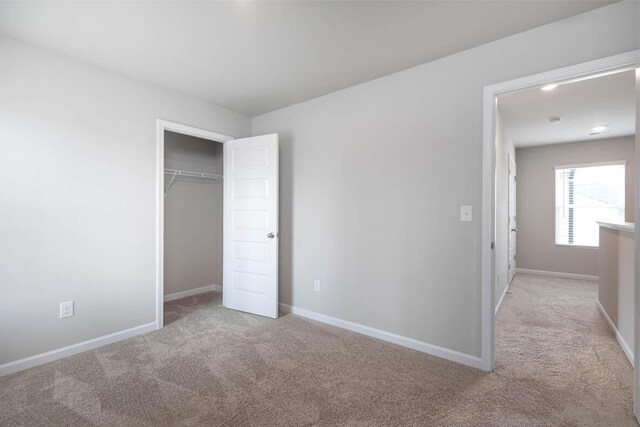 unfurnished bedroom featuring light carpet, a closet, and baseboards