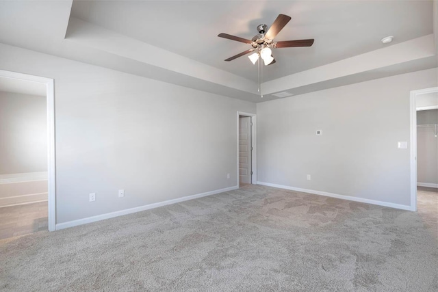 carpeted empty room with a raised ceiling, ceiling fan, and baseboards