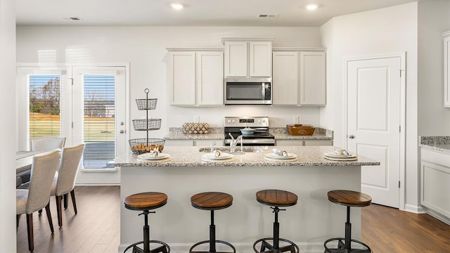 kitchen featuring visible vents, stainless steel appliances, dark wood-type flooring, and a kitchen breakfast bar