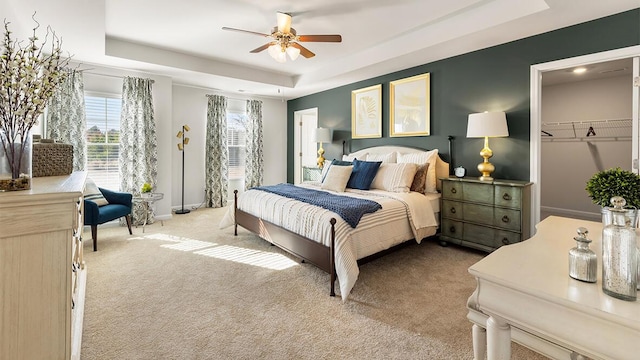 carpeted bedroom with a walk in closet, a raised ceiling, ceiling fan, and baseboards