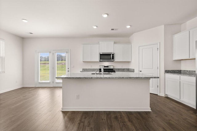 kitchen with white cabinets, appliances with stainless steel finishes, light stone counters, dark wood-type flooring, and a kitchen island with sink