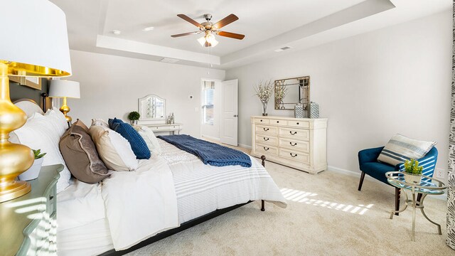 carpeted bedroom with a ceiling fan, a raised ceiling, visible vents, and baseboards