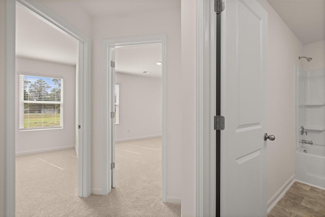 corridor with baseboards and light colored carpet