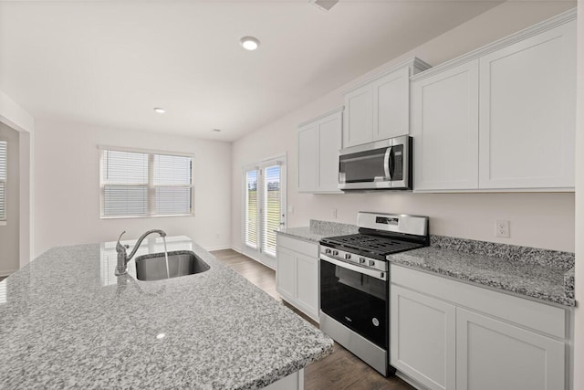 kitchen featuring dark wood-style floors, stainless steel appliances, white cabinets, a sink, and light stone countertops