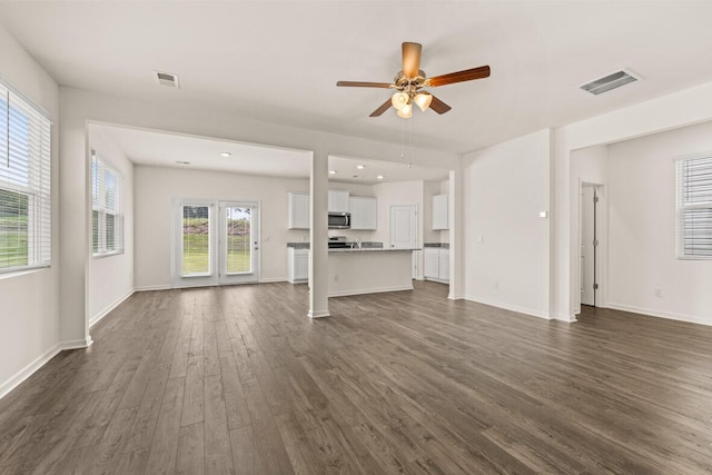 unfurnished living room with baseboards, visible vents, ceiling fan, and dark wood-type flooring