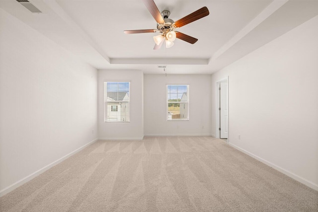 spare room featuring light carpet, visible vents, a tray ceiling, and baseboards