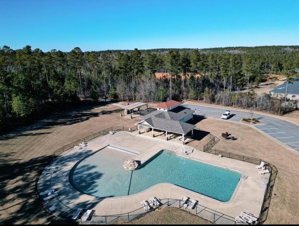 community pool with fence, a view of trees, and a patio