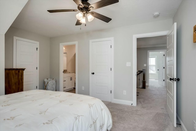 bedroom featuring light carpet, ceiling fan, ensuite bathroom, and baseboards