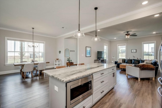 kitchen with pendant lighting, white cabinets, stainless steel microwave, and light stone countertops