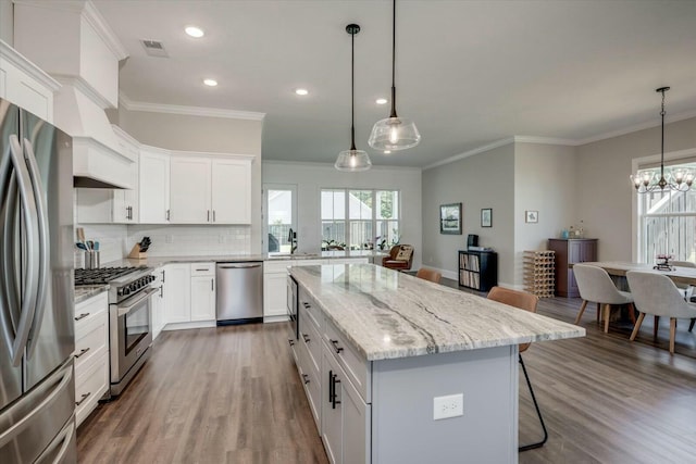 kitchen featuring white cabinets, a kitchen island, appliances with stainless steel finishes, a breakfast bar, and pendant lighting