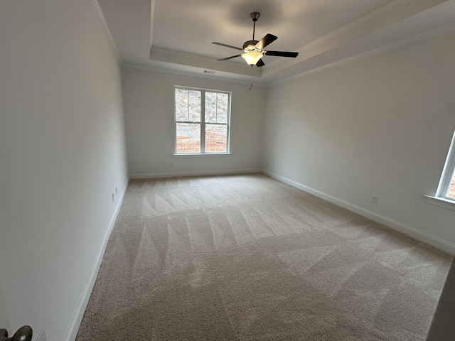 empty room featuring baseboards, a tray ceiling, ornamental molding, and light colored carpet