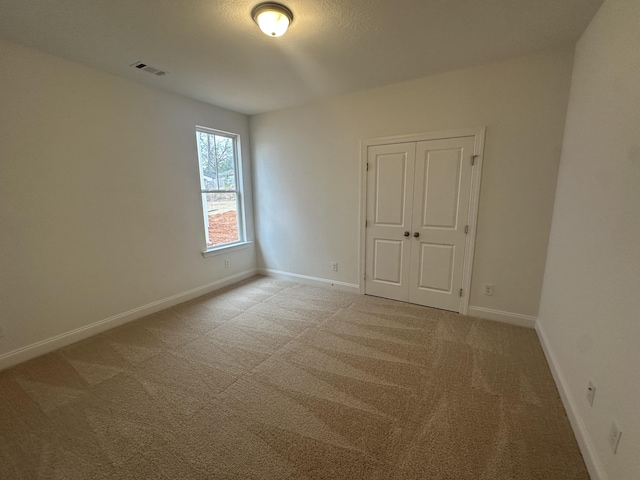 spare room featuring carpet floors, visible vents, and baseboards