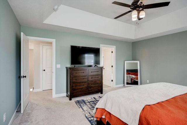 bedroom with a raised ceiling, light colored carpet, and ceiling fan