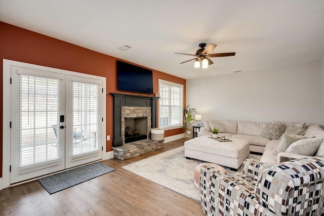 living room with a stone fireplace, hardwood / wood-style floors, ceiling fan, and french doors