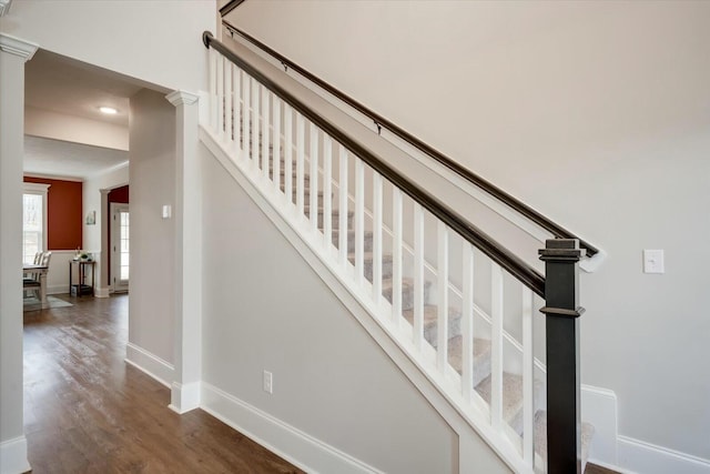 staircase with ornate columns, wood-type flooring, and ornamental molding