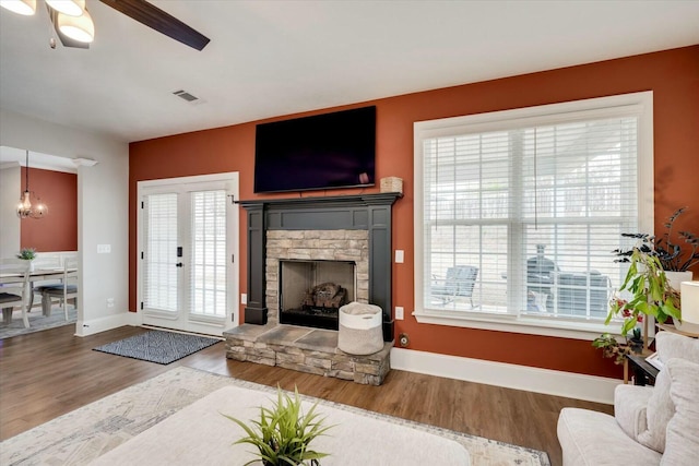 living room with ceiling fan with notable chandelier, a fireplace, and hardwood / wood-style floors