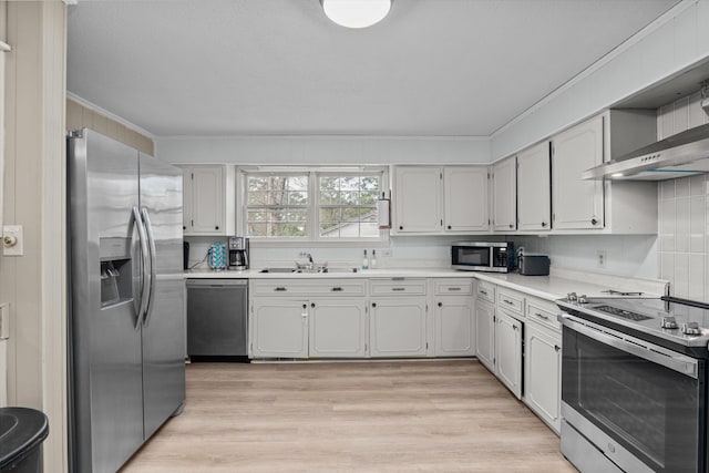 kitchen with appliances with stainless steel finishes, sink, wall chimney range hood, and white cabinets