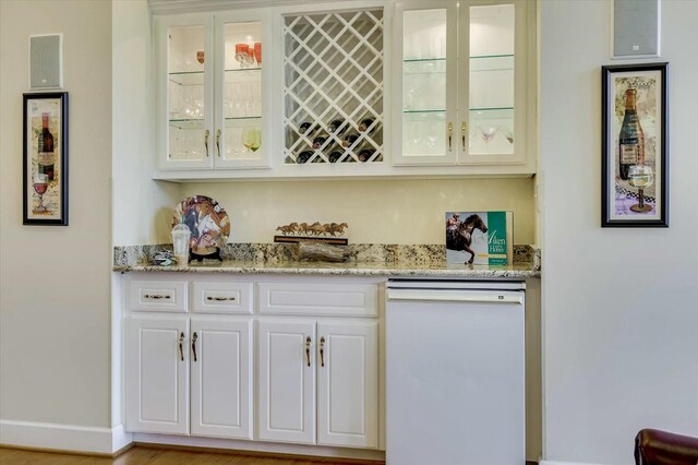 bar with white dishwasher, light stone counters, and white cabinetry