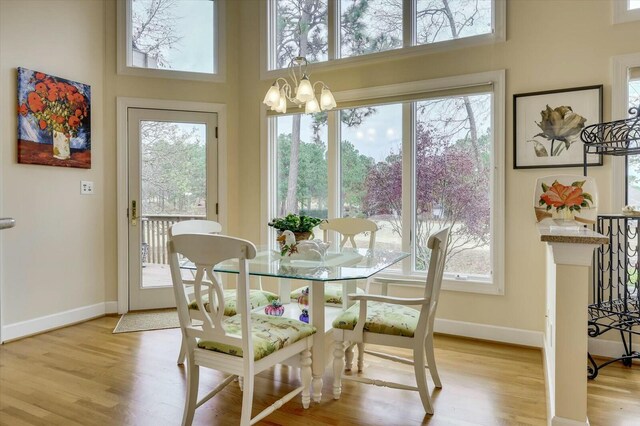 dining room with light hardwood / wood-style flooring, a towering ceiling, a healthy amount of sunlight, and an inviting chandelier