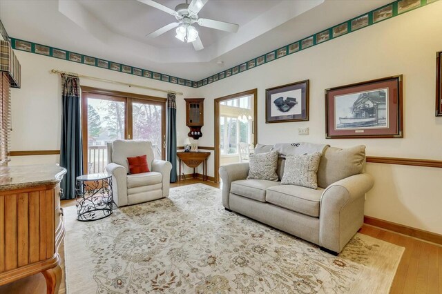 living room featuring light wood-type flooring, a raised ceiling, and ceiling fan