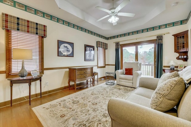 living room with wood-type flooring, a tray ceiling, and ceiling fan