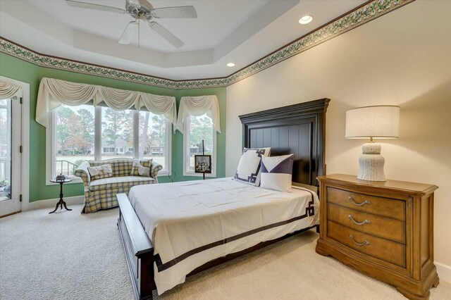 bedroom featuring light carpet, a tray ceiling, and ceiling fan