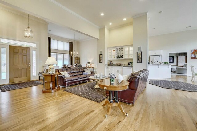 living room featuring a high ceiling, light hardwood / wood-style floors, an inviting chandelier, and crown molding