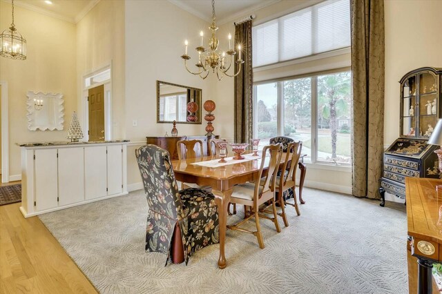 dining space featuring a high ceiling, light wood-type flooring, an inviting chandelier, and crown molding