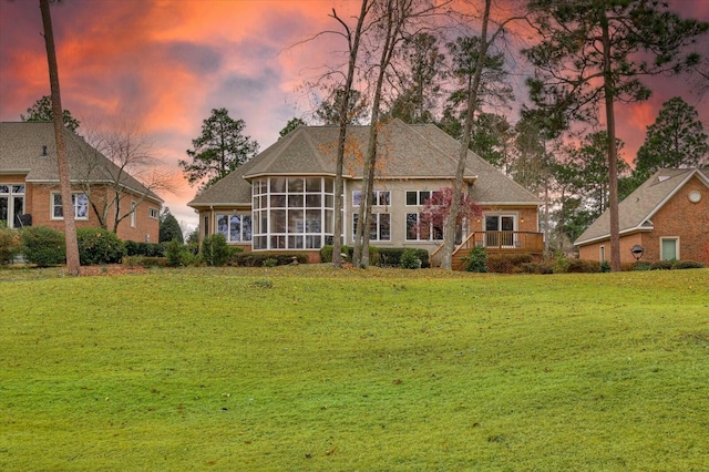 back house at dusk with a sunroom and a yard