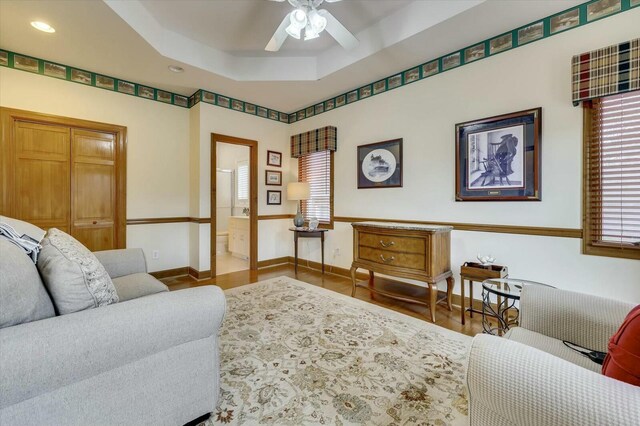 living room with hardwood / wood-style floors, a tray ceiling, and ceiling fan