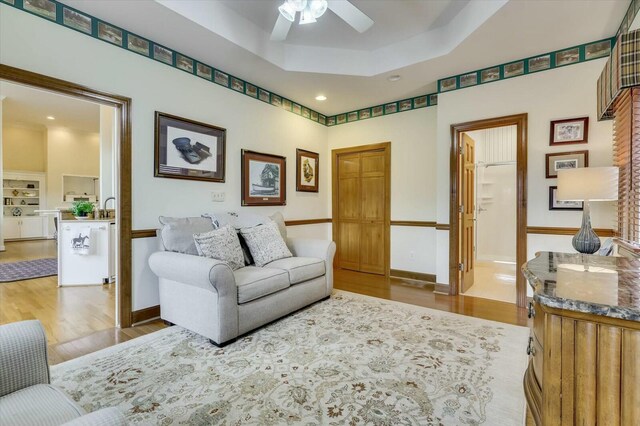 living room with hardwood / wood-style floors, ceiling fan, and a raised ceiling