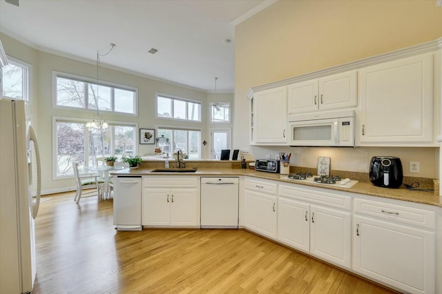 kitchen with white appliances, an inviting chandelier, sink, decorative light fixtures, and white cabinetry