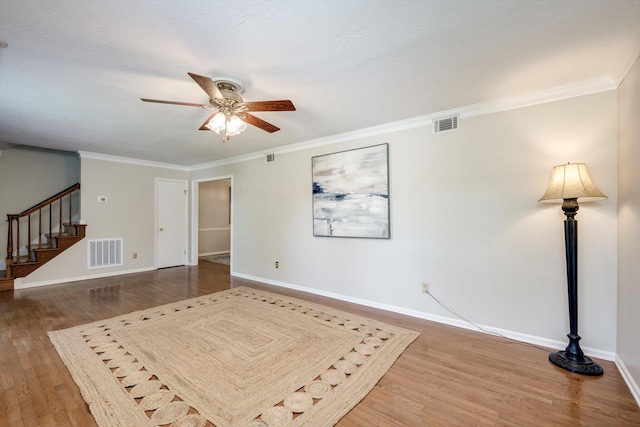 unfurnished living room with wood finished floors, ceiling fan, baseboards, stairs, and crown molding