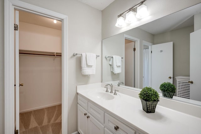 full bath with vanity, a walk in closet, and baseboards