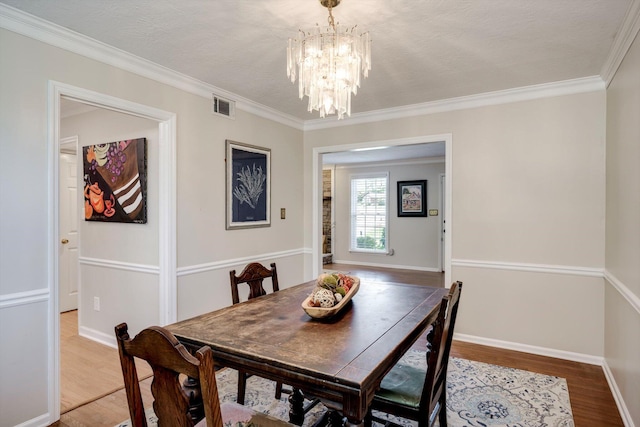 dining room with wood finished floors, a chandelier, crown molding, and baseboards