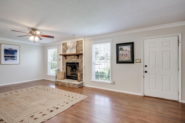 unfurnished living room featuring ornamental molding, wood finished floors, a stone fireplace, baseboards, and a ceiling fan