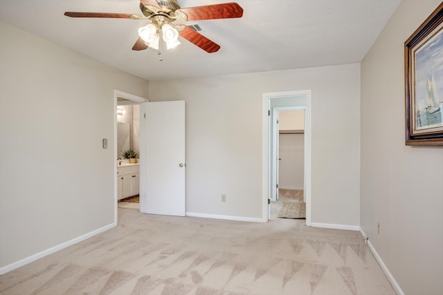 unfurnished bedroom featuring light colored carpet, a walk in closet, baseboards, and a ceiling fan