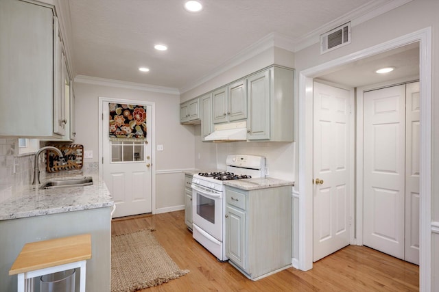 kitchen featuring white gas stove, a sink, ornamental molding, under cabinet range hood, and light wood-style floors