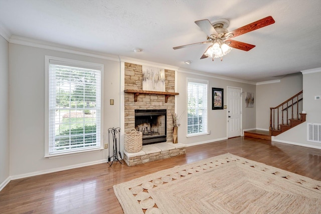 unfurnished living room featuring wood finished floors, crown molding, baseboards, and a stone fireplace