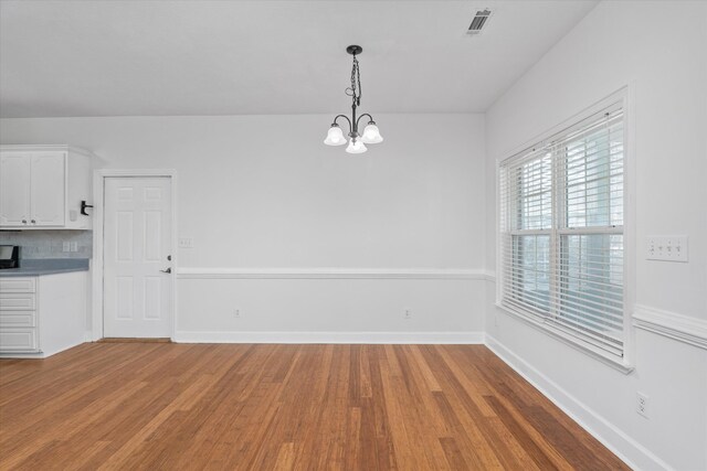 unfurnished dining area with an inviting chandelier and hardwood / wood-style floors