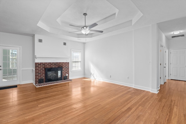 unfurnished living room featuring a fireplace, plenty of natural light, light hardwood / wood-style floors, and a raised ceiling