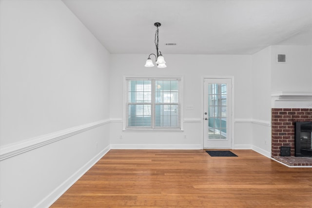 unfurnished dining area featuring an inviting chandelier, hardwood / wood-style flooring, and a fireplace