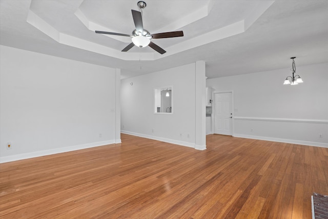 unfurnished living room featuring ceiling fan with notable chandelier, a tray ceiling, and light hardwood / wood-style floors