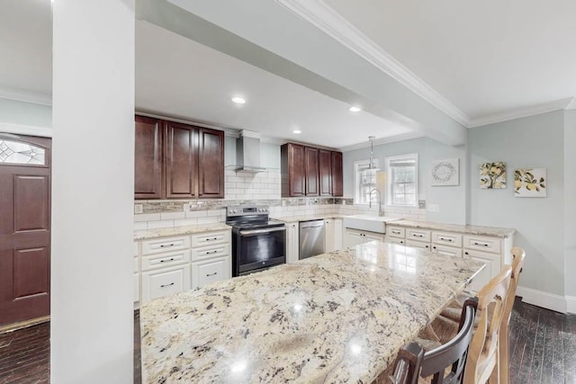 kitchen with sink, appliances with stainless steel finishes, white cabinetry, a kitchen bar, and wall chimney exhaust hood