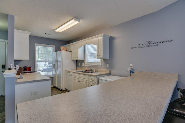 kitchen with white appliances, kitchen peninsula, sink, a textured ceiling, and white cabinetry