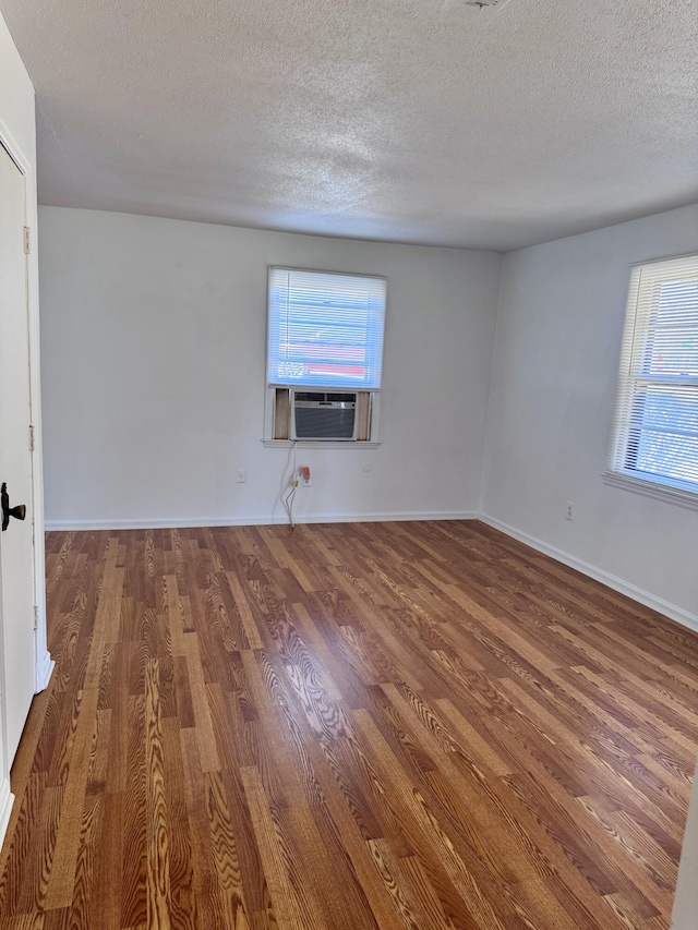 empty room with a textured ceiling, cooling unit, and dark wood-type flooring