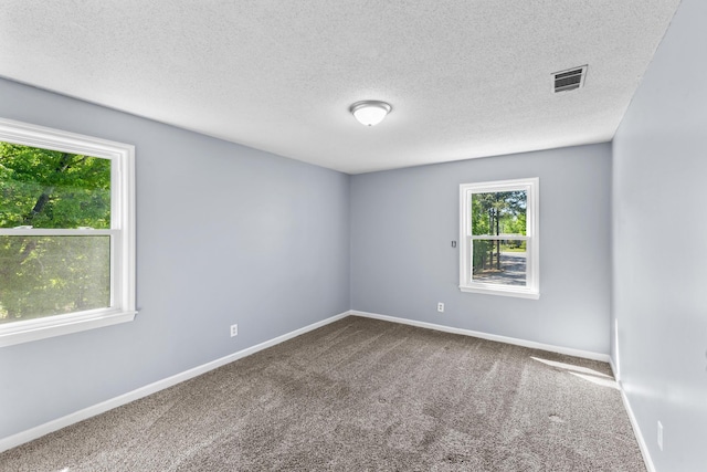 empty room with carpet flooring, visible vents, a textured ceiling, and baseboards