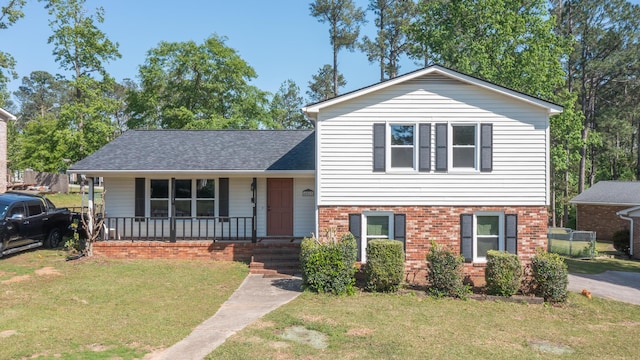 tri-level home featuring a front yard, a porch, a shingled roof, and brick siding